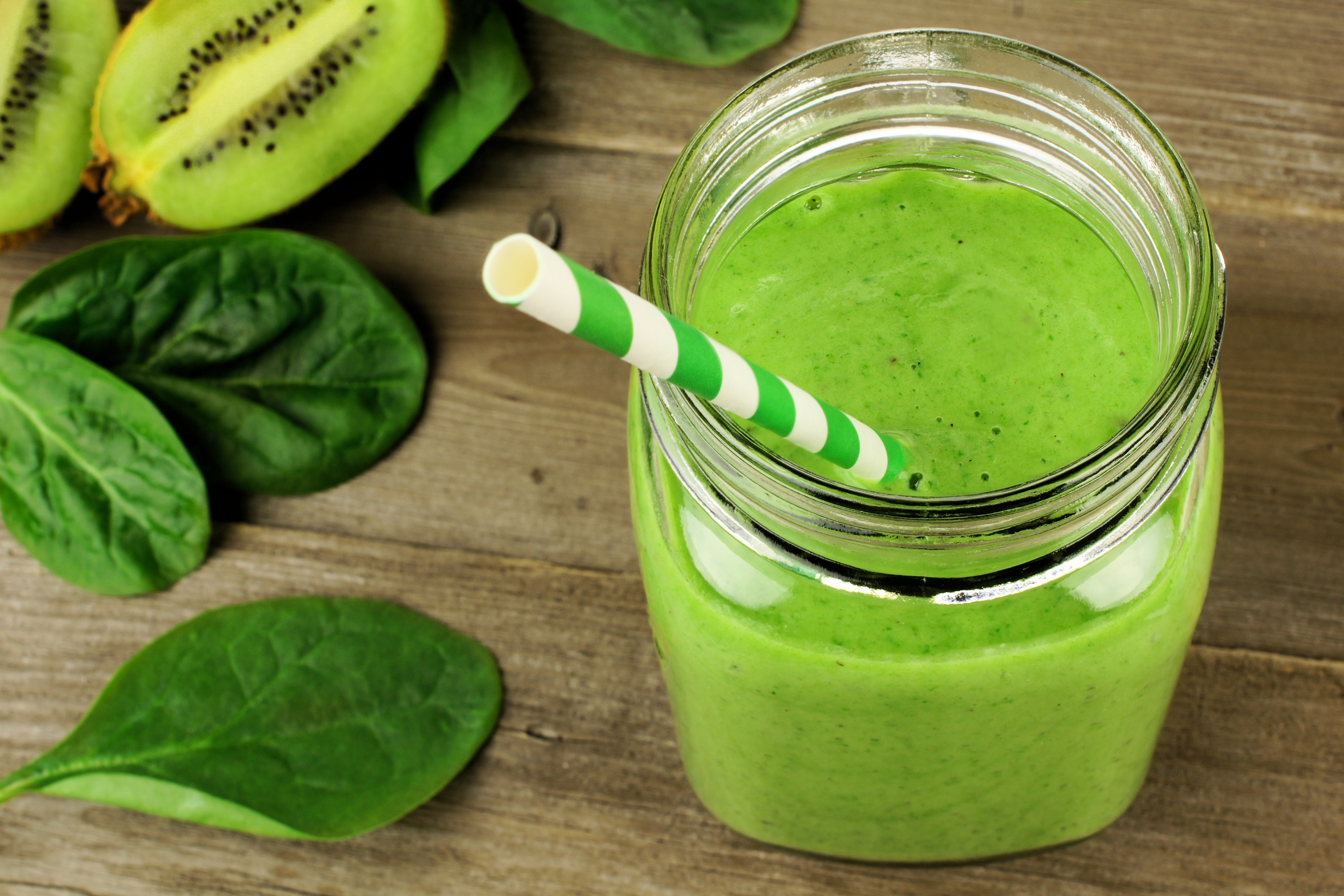 Healthy green smoothie with spinach and kiwi in a jar mug on wood, downward view